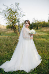 Bride in a white wedding dress standing in a garden, holding a bouquet of white roses. Warm sunlight creates a romantic atmosphere full of tenderness and serenity.