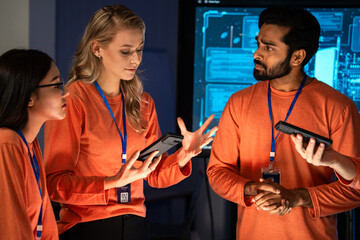 Diverse tech team discus about digital security using smartphones in a high-tech control room. Female colleague sharing idea in the meeting. Professionals are collaborating on mobile technology 