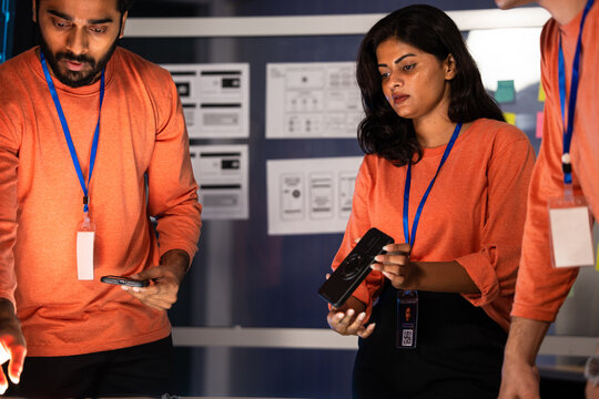 Cybersecurity team working late night in a dark operations center. Collaborating on an urgent data investigation using mobile technology for a digital security analysis. Project meeting and brainstorm