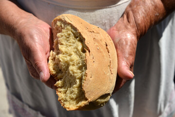 A close-up, atmospheric photograph capturing the skilled hands of an artisan breaking apart freshly baked, crusty bread