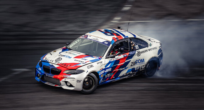 Latvia, Riga 03-05.10.2025. FIA Drifting cup,  a BMW M5 drifting on a track with smoke coming out of it, wearing a helmet and surrounded by a blurred background