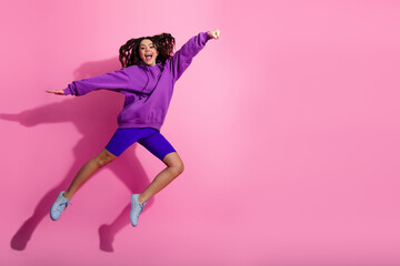 Energetic young woman in purple sportswear jumping joyfully against a vibrant pink background,...
