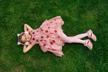 A girl wearing headphones and glasses is lying on the grass. cheerful child is playing and laughing in the park.