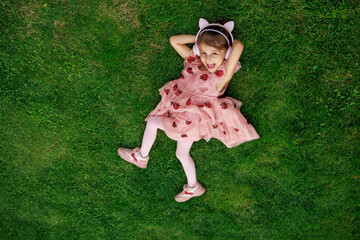 A girl wearing headphones and glasses is lying on the grass. cheerful child is playing and laughing in the park.