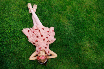 A girl with glasses is lying on the grass. A cheerful child is playing and laughing in the park.