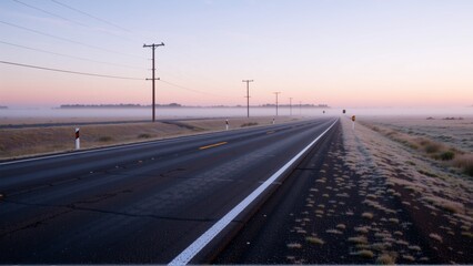 Fototapeta premium long straight road white line marking center road road surrounded dry grass shrubs both sides side highway power lines telephone poles sky pale pink color indicating either sunrise sunset distance