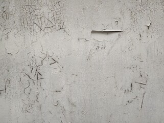 Light gray background, peeling cracked paint. A close-up view of a wall reveals an intricate pattern of cracks and peeling paint. The texture conveys a feeling of age and weathering.