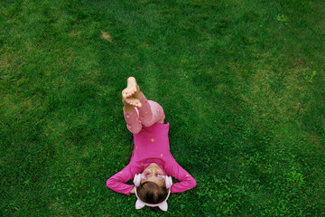 A girl wearing headphones and glasses is lying on the grass. cheerful child is playing and laughing in the park.