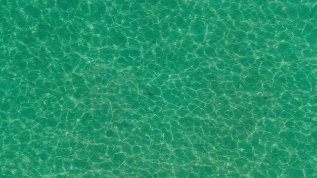 Drone view of sea water pattern reflecting sunrays on white sand