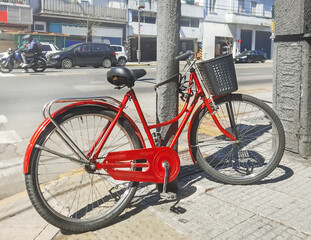 A red bicycle parked by the road and locked to a pole.