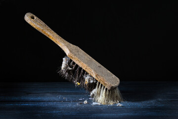 Old hand brush with worn wooden handle and natural bristles with many dust bunnies, standing against a dark background, still life, vintage cleaning utensil, copy space, selected focus