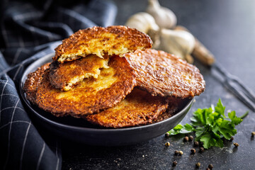 Fried potato pancake on plate on black table.