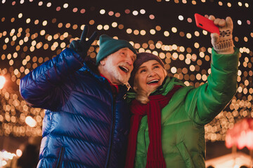 Funny heartwarming winter selfie with grandparents under twinkling Christmas lights at a festive outdoor market