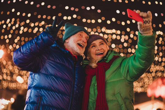 Funny heartwarming winter selfie with grandparents under twinkling Christmas lights at a festive outdoor market