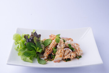 Spicy Squid Salad, a Thai dish. Long, white squid squid tossed in a dressing, mint, basil, and salad greens on a white plate.