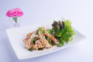 Spicy Squid Salad, a Thai dish. Long, white squid squid tossed in a dressing, mint, basil, and salad greens on a white plate.
