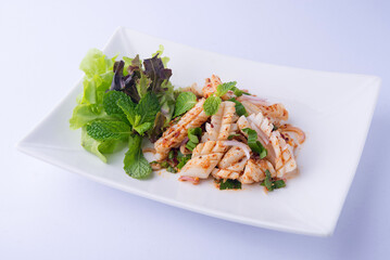 Squid salad: Squid with stripes, basil, and peppermint leaves, and a spicy, clear yellow dressing. Salad greens on a white plate.