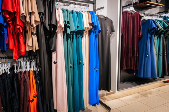 Colorful dresses neatly hung on racks in a clothing store, featuring a variety of shades including red, beige, teal, blue, black, and burgundy velvet.