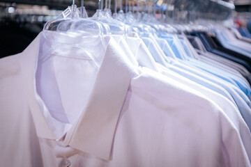 Neatly arranged men's dress shirts in shades of white, blue, gray, and black on clear plastic hangers in a clothing store.