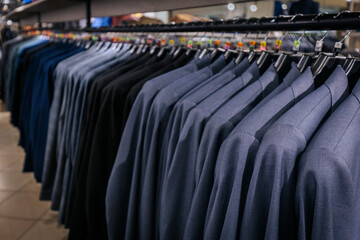 Row of neatly hung grey blue mens blazers on black hangers in a clothing store, arranged by size...
