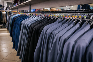 Fototapeta premium Row of neatly hung grey blue mens blazers on black hangers in a clothing store, arranged by size for a polished and professional presentation.