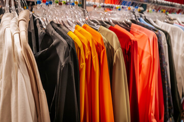 Fototapeta premium A colorful selection of tops and dresses on display in a clothing store, neatly arranged on clear plastic hangers for a vibrant shopping experience.