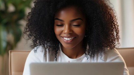 Smiling woman working on a laptop, surrounded by modern office decor. Theme of digital technology and business success.