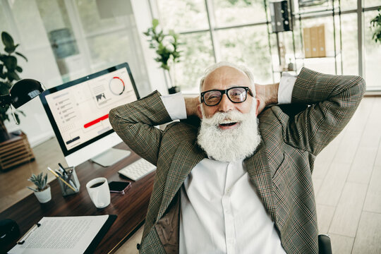 Senior businessman relaxing at desk in office with computer, displaying professional success and confidence