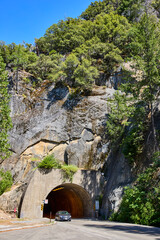 Tunnel Entrance Road and Car Surrounded by Rocky Cliffs and Lush Green Forest