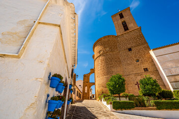 Charming Spanish Street with Blue Flower Pots and Historic Stone Church Tower under Bright Blue Sky