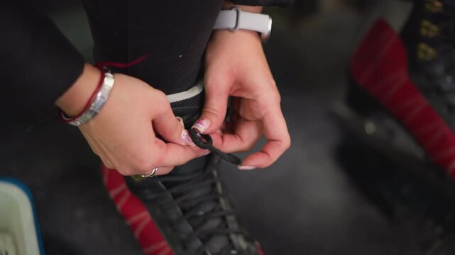 Lady putting on red black ice skates tightening laces with detailed view of hands and fingers pulling strings preparing for skating activity showing focus determination and readiness for winter sport