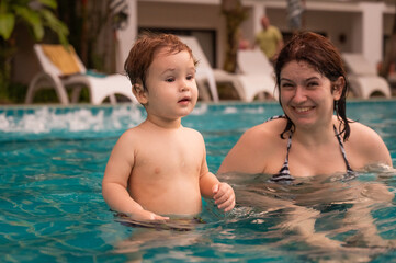 Caucasian woman holds her son while swimming in a pool on vacation. Mom teaches little boy to swim. 