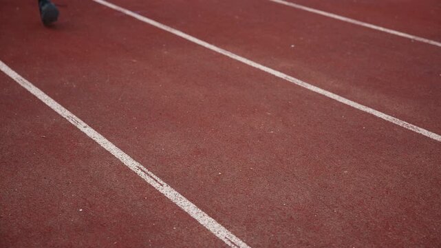 Athlete with a disability, wearing a prosthetic running blade, pausing on the track to tie his shoelace on a sneaker, close up. Motivation and persistence concept.