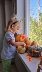 A child decorates pumpkins on a windowsill for the autumn holidays of Halloween and Thanksgiving.