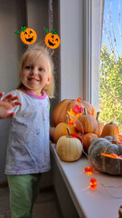 A child decorates pumpkins on a windowsill for the autumn holidays of Halloween and Thanksgiving.