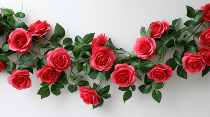 Obraz premium Beautiful arrangement of vibrant red roses with lush green leaves delicately cascading across a clean white surface creating a visually appealing floral display.