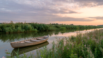 Obraz premium River Scene at Dusk with a Rustic Teal Boat, Lush Ferns, and a Beautiful Blend of Sunset Colors - tranquil nature image