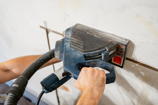 Electrician holding wall chaser power tool while cutting groove for electrical wires in concrete wall, concept of renovation, precision, and professional construction work.
