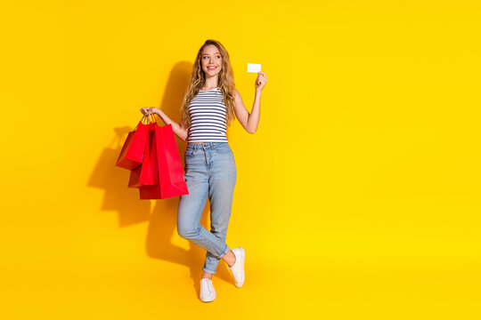 Cheerful young woman with shopping bags and credit card against a vibrant yellow background enjoying a successful shopping spree