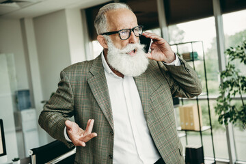 Senior professional engaged in a focused business call at an office workspace with modern decor and natural lighting