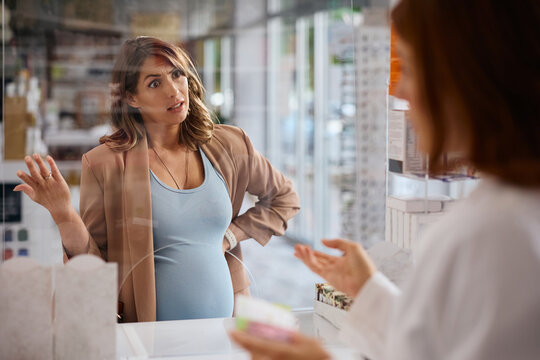 Displeased pregnant woman talking to pharmacist in drugstore.
