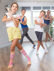 Fototapeta premium Active tween girl training dance positions with her parents and brother in light room during workout session
