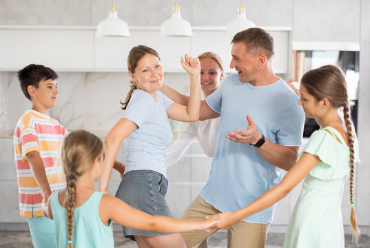 Children stand around their dancing parents in kitchen. Family holiday, important event.