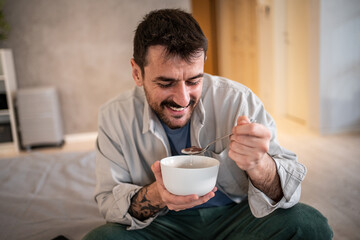Happy man eating cereal for breakfast in bed
