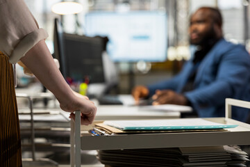 Close up of woman archivist moves a trolley stacked with documents files and records, offers assistance with workplace support administrative tasks. Bringing folders from the company archive.