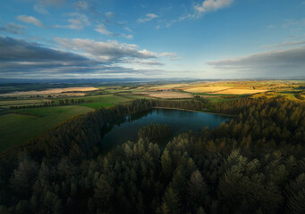 Aerial drone photo of forest lake and countryside fields at sunset. Scenic rural landscape with trees and golden light. Beecraigs Country Park, West Lothian, Scotland