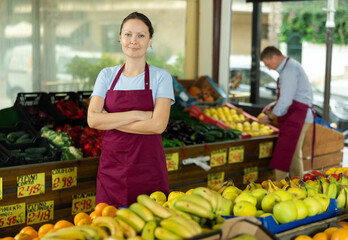 Positive and friendly store woman employee stands with arms crossed on chest and waits for customers. Greengrocers shop, products from local farmer, eco-food