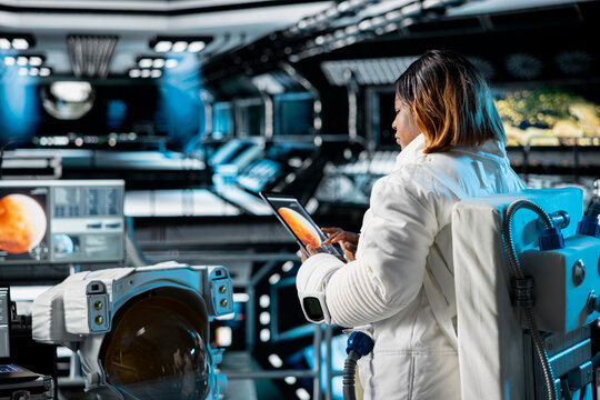 Female astronaut in orbital station analyzing Mars planetary data on tablet. Crew member in spaceship doing Martian surface research using device to assist future planetary exploration