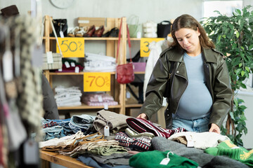 Pregnant woman chooses warm winter sweater in a clothing store