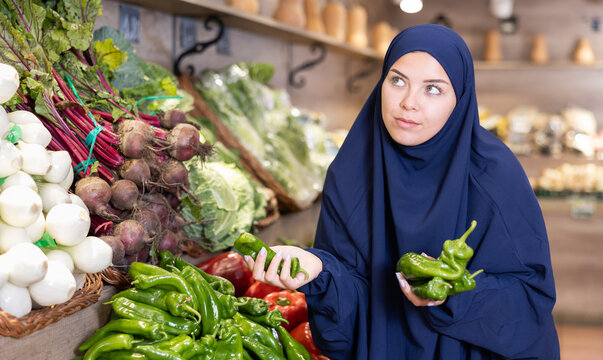 Portrait of girl in paranja buying fresh bell peppers in grocery shop